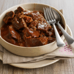 Morceaux de bœuf à braiser, coupés en cubes et légèrement farinés, près des autres ingrédients.