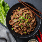 Bœuf Bulgogi saisi à feu vif dans un wok, avec des morceaux d'oignon, fumant.