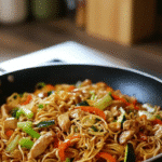 Un Wok de Poulet aux Nouilles et Légumes fumant, prêt à être servi, avec des cébettes fraîches. Wok de Poulet aux Nouilles et Légumes